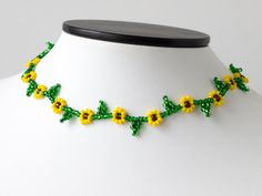 a green and yellow beaded necklace on a white mannequin neckpiece with flowers