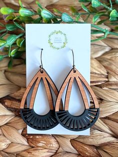 wooden earrings with black and brown accents on a card next to some leaves in the background