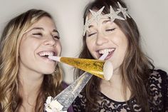 two young women are smiling and one is holding a toothbrush in her mouth while the other holds a fake bird's head