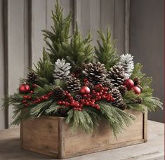 a wooden box filled with pine cones and red berries on top of a wood table