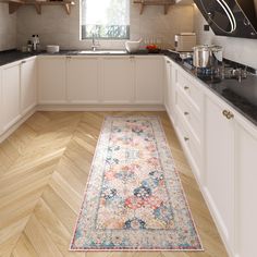 a kitchen with white cabinets and wooden floors, an area rug in the middle of the floor