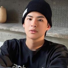 a young man wearing a beanie sitting in front of a counter with his arms crossed