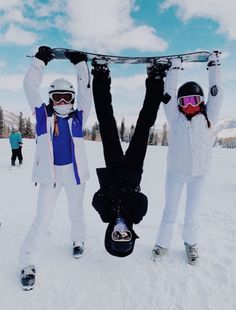 two snowboarders hold their boards above their heads while standing in the snow on skis