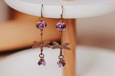 a pair of dragonfly earrings with purple crystals hanging from it's earwires