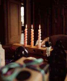 three lit candles sitting on top of a wooden table next to a wine bottle and other items