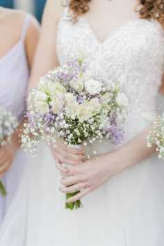 two bridesmaids holding bouquets of white and purple flowers in their hands,