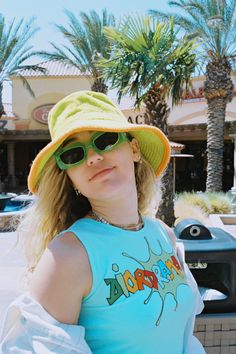 a woman wearing sunglasses and a hat standing next to a parking meter with palm trees in the background