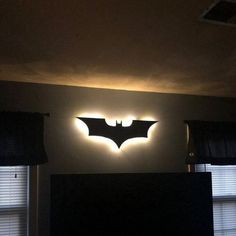 the batman logo is lit up on the wall above the bed in this dark room