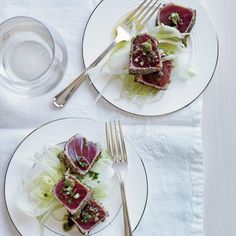 two white plates topped with food next to silver utensils and a glass of water