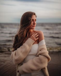 a woman standing on the beach with her hair blowing in the wind and looking off into the distance