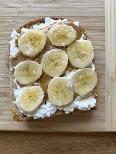 a piece of bread topped with bananas and cream on top of a wooden cutting board