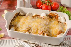 a casserole dish with cheese and tomatoes on the table next to some utensils