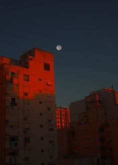 the moon is setting over an apartment building with red light reflecting off it's windows