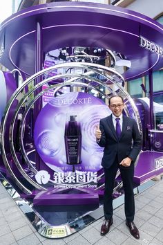 a man in a suit and tie standing next to a purple display with an advertisement on it