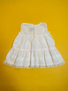 "An original vintage 1960s/1970s white voile baby girls dress. This pretty dress is made from a Terylene voile synthetic fabric with white floral lace detailing. It has a pink ribbon at the hips which is threaded through the lace. The neckline and armholes are edged in narrow white lace and it is fastened with two ties at the back. It is labelled 'Made in England'. The dress is in excellent condition with no marks or damage. There is no size label in the garment but it fits approximately 9-12 months. Please note all measurements below have been measured flat. Please compare these measurements to something you already own to compare sizing. Measurements: Chest: 22\" 56cms Shoulder to Shoulder: 8.5\" 21.5cms Length: 16\" 40.5cms" Cute White Vintage Dress With Lace Trim, Sleeveless Cotton Baptism Dress With Ruffles, Sleeveless Cotton Baptism Dress For Spring, Sleeveless Cotton Baptism Dress For Summer, Cute Sleeveless Baptism Dress With Ruffles, Sleeveless Cotton Baptism Dress, Spring Sleeveless Baptism Dress, White Sleeveless Cotton Baptism Dress, White Sleeveless Baptism Dress For Summer