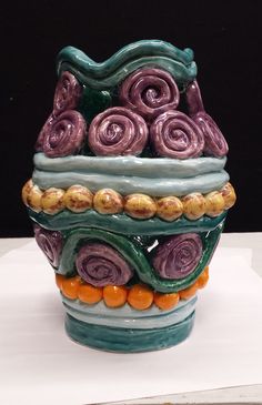 a ceramic vase sitting on top of a white table next to an orange and purple object