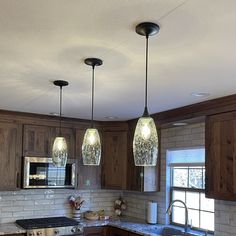 three lights hanging from the ceiling in a kitchen with granite counter tops and wooden cabinets