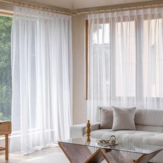 a living room filled with furniture and windows covered in white sheer curtaines next to a wooden coffee table