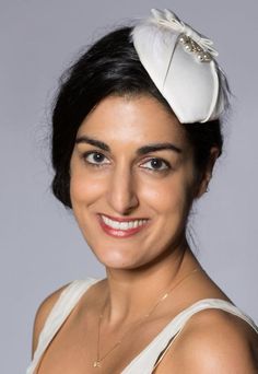 This unique deco bridal hat is strongly influenced by 1930s styling and takes elements from vintage bridal pieces. It was created with lightly padded off-white satin over a lightweight straw base, with a hand stitched soft feather trim and a glass bead and silver wire decoration. The piece is completed with a tailored satin bow. The reverse is finished with traditional millinery petersham and a comb bound with satin ribbon. The hat is 12.5cm at the widest point and 15cm long. The comb will sit s Elegant Fascinator Headband For Vintage Events, Elegant Headband Fascinator For Vintage Events, Gatsby Style Wedding Headband Hat, Cream Gatsby Hat For Wedding, Elegant White Hats For Vintage Events, Elegant White Hat For Vintage Events, Gatsby Style Mini Hat Headband For Weddings, Elegant Hats For Vintage Events, Elegant White Costume Hats For Ceremonies