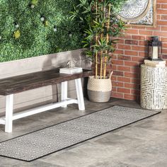 a wooden bench sitting next to a brick wall and potted plant on top of a rug