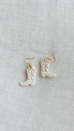 two pairs of white ceramic cowboy boots hanging from gold earwires on a gray background