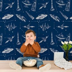 a young boy sitting on the floor in front of a blue wall with spaceships and stars