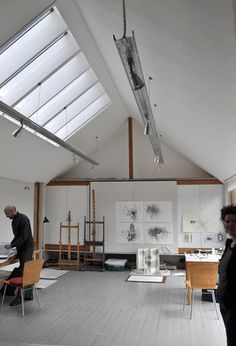 two people standing in an art studio looking at artwork on the walls and ceiling,