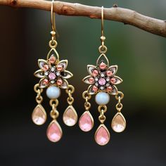 two pairs of pink and blue earrings hanging from a tree branch on a sunny day