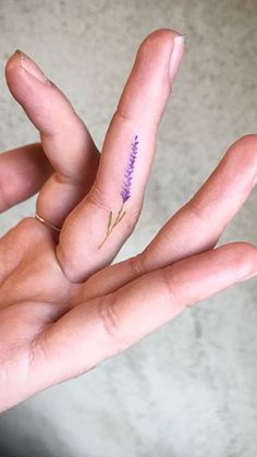 a person's hand with a tiny flower tattoo on the middle finger and two fingers