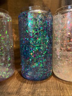 three jars filled with glitter sitting on top of a wooden table