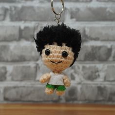 a crocheted doll hanging from a keychain with a brick wall in the background