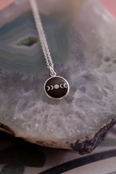 a silver necklace with three phases on it sitting on top of a piece of rock