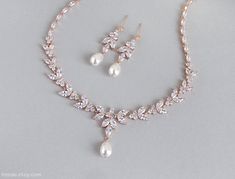 a necklace and earring set with pearls on a gray background for a bridal look