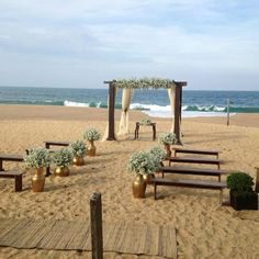 an outdoor ceremony setup on the beach with flowers and greenery in vases at the end