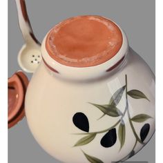 a tea pot with a spoon in it on a gray background and the lid is decorated with leaves