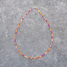 a multicolored beaded necklace is displayed on a gray surface with a silver chain