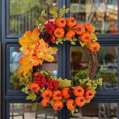 an orange wreath with berries and leaves is hanging on the window sill in front of a store