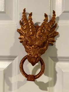 a golden door handle with an intricately carved face on it's side, in front of a white door