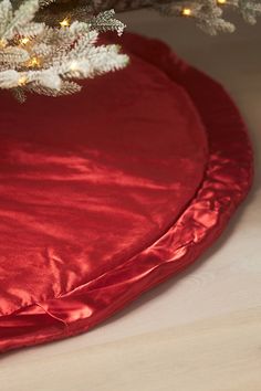 a christmas tree skirt is on the floor next to a red round pillow under a white christmas tree