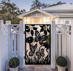 an iron gate with flowers and butterflies on it in front of a white picket fence