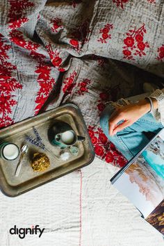 a person laying in bed next to a tray with food on it and an open magazine