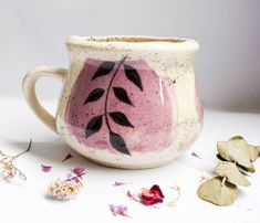 a white and pink coffee cup sitting on top of a table next to dried flowers