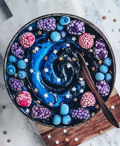 a bowl filled with blue and purple cake next to a wooden spoon on top of a cutting board