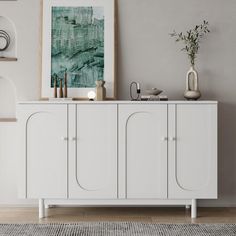 a white sideboard with two vases on top and a painting hanging above it