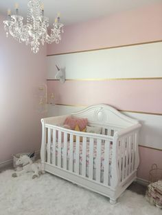 a baby's room with pink walls and white crib in the corner, chandelier hanging from the ceiling