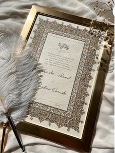 a white feather laying on top of an ornate frame next to a pen and paper