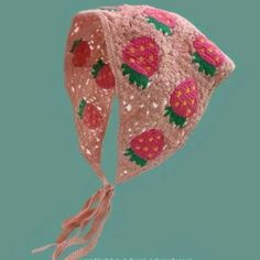 a pink crocheted hat with strawberries on the front and side, hanging from a string