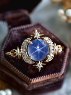 a blue ring sitting on top of a purple velvet box with stars and diamonds around it