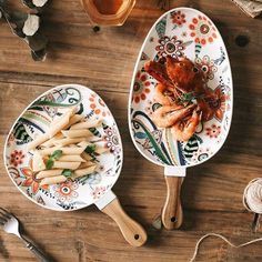 two serving spoons with food on them sitting on a wooden table next to other utensils