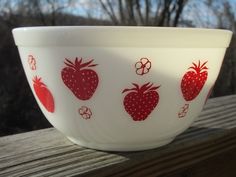 a red and white bowl with strawberries on it sitting on a wooden table outside